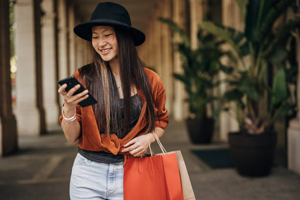istock Young fashionable asian woman using mobile phone while shopping 1401739493