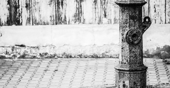 Very old warn green out of order street water pump standing alongside pavement with copy space, black and white image