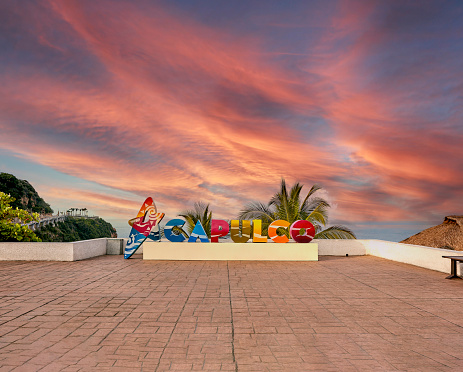 Beautiful colorful Acapulco inscription sign with bright colorful letters and blue ocean and trees as background