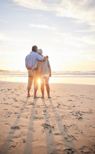 Loving senior couple watching a sunset on a sandy beach stock photo