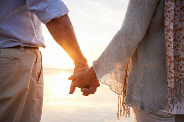 istock Senior couple standing hand in hand on a beach at sunset 1401741509