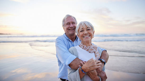 istock Senior couple laughing while standing together on a beach at sunset 1401742950