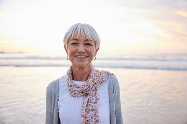 istock Smiling senior woman standing on a beach at sunset 1401743037