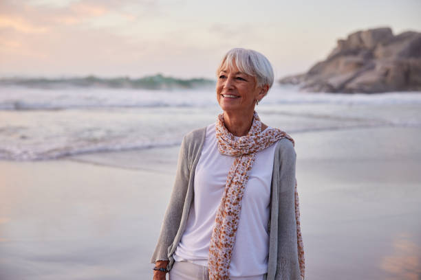 istock Senior woman smiling while walking on a beach at sunset 1401743484