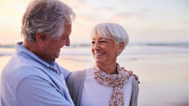 istock Senior woman laughing while standing with her husband on a beach at sunset 1401744456