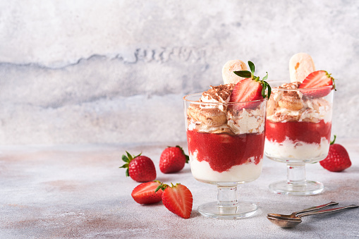 Strawberry tiramisu. Traditional Italian dessert tiramisu in glass with fresh strawberry and mint leaves on old gray concrete background table background. Copy space. Food background.