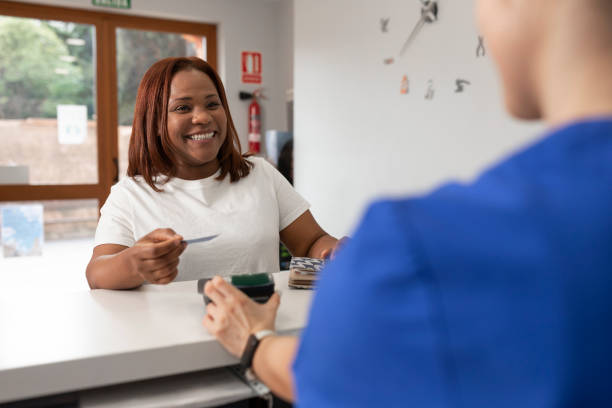 чернокожая женщина улыбается от радости, держа в руках св�ою кредитную карту, прежде чем заплатить в обмен на хорошее обслуживание, которое � - dentist office clinic dentist office стоковые фото и изображения