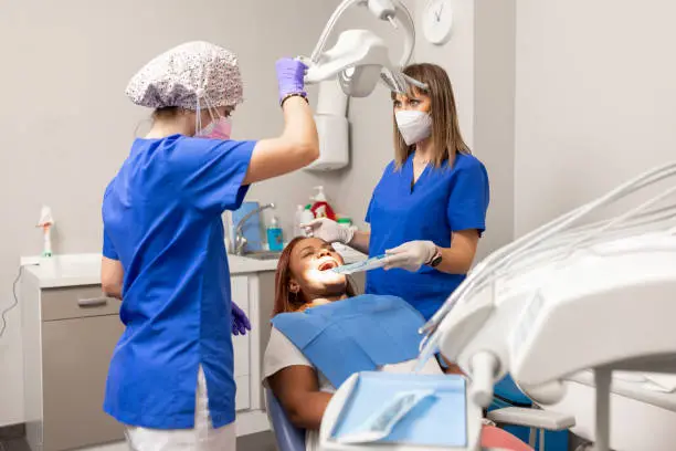 Photo of The dentist woman adjust the dental operating light, while the client lays in the dental chair with her mouth open at the dental clinic