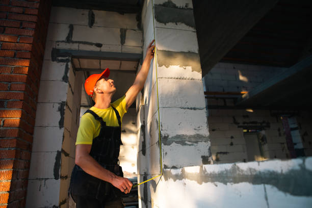 istock Construction worker at construction site measures the length of window opening and brick wall with tape measure. Cottage are made of porous concrete blocks, work clothes - jumpsuit and baseball cap 1401749161