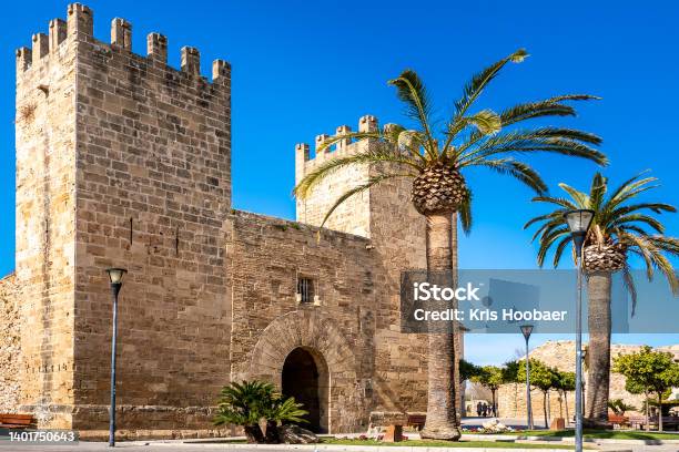 Historic Alcúdia City Gate Called Porta Del Moll Also Known As Porta De Xara With Palm Trees In The Foreground And The Old Alcudia City Wall In The Background On A Sunny Springtime Day With Blue Sky Stock Photo - Download Image Now