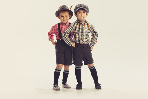 Portrait of two little boys, children in retro style clothes posing, looking at camera isolated over grey studio background. Concept of childhood, friendship, family, fun, lifestyle, fashion