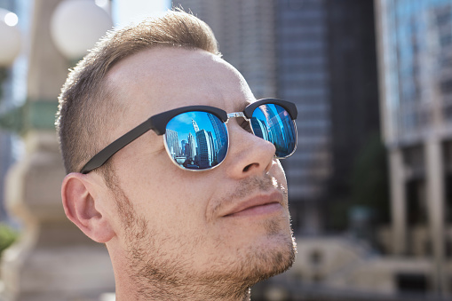 Reflection of skyscrapers in sunglasses of young man. Tourist admiring historical buildings in city. Themes of tourism and eye protection.\