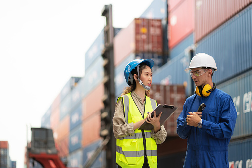 Dock manager and engineer worker in safety helmet discussing in shipping container yard with copy space. Import and export product. Manufacturing transportation and global business concept