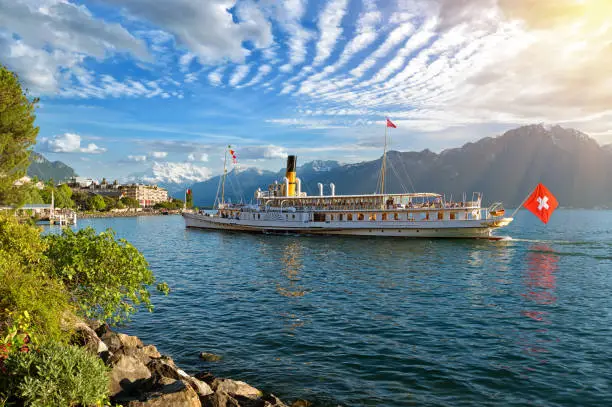Beautiful summer evening landscape of Lake Geneva with picturesque shores and pleasure ship against Alpine mountains in the rays of the setting sun in Montreux, Switzerland