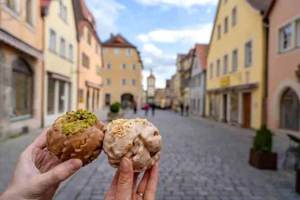 eating traditional schneeball snowball cake together the cake of the romantic Rothenburg ob der Tauber with timbered Fachwerkhaus syle houses in Bavaria Germany .