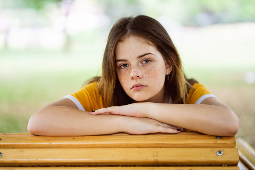 Portrait of redhead Caucasian teenage girl, with blue eyes and freckles leaning on the picnic table