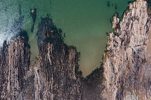 Looking directly down on to a section of rocky coastline from a drone on a bright summer morning