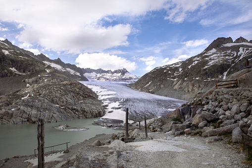 Scenic view on Rhone Glacier in swiss Alps with the lake. High mountains landscape, arid terrain of Rhonegletscher, mountain trail in Switzerland.