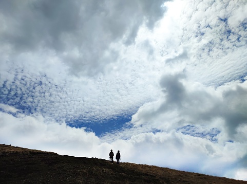Two hikers silhouettes in mountains against cloudy sky