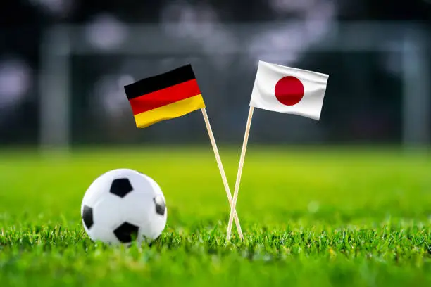 Photo of Germany vs. Japan, Khalifa Stadium, Football match wallpaper, Handmade national flags and soccer ball on green grass. Football stadium in background. Black edit space.