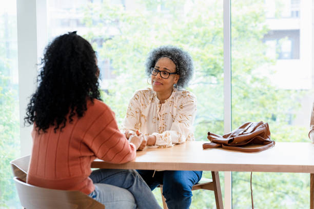 Senior mother consoles unrecognizable adult daughter When they meet at the coffee shop, the senior adult mom consoles her unrecognizable adult daughter as she reaches out to hold her daughter's hands. empathy stock pictures, royalty-free photos & images