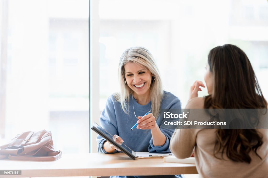 Female financial advisor reviews documents on digital tablet Meeting with the unrecognizable female client, the mature adult female financial advisor goes over documents on the digital tablet. Financial Advisor Stock Photo