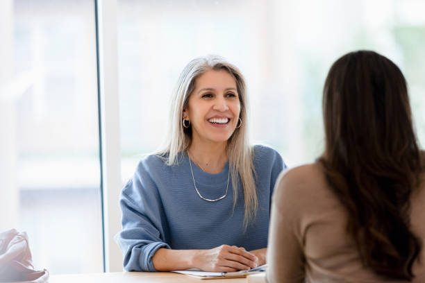 Female lawyer smiles while listening to unrecognizable female client The mature adult female lawyer smiles as she listens to the unrecognizable female client. lawyer stock pictures, royalty-free photos & images
