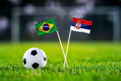 Brazil vs. Serbia, Lusail, Football match wallpaper, Handmade national flags and soccer ball on green grass. Football stadium in background. Black edit space.