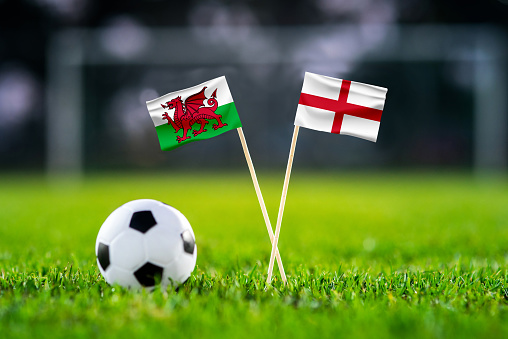 Wales vs. England, Ahmad Bin Ali, Football match wallpaper, Handmade national flags and soccer ball on green grass. Football stadium in background. Black edit space.