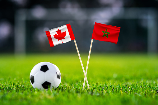 Canada vs. Morocco, Al Thumama, Football match wallpaper, Handmade national flags and soccer ball on green grass. Football stadium in background. Black edit space.