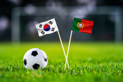 South Korea vs. Portugal, Education City, Football match wallpaper, Handmade national flags and soccer ball on green grass. Football stadium in background. Black edit space.