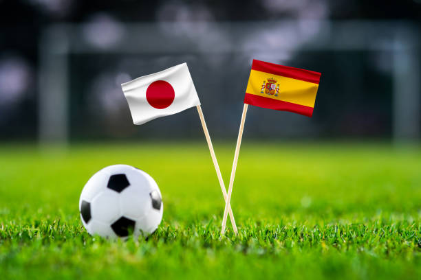 日本対スペイン、ハリファスタジアム、サッカーの試合の壁紙、手作りの国旗と緑の芝生の上のサッカーボール。背景にサッカースタジアム。黒い編集スペース。 - 日本　スペイン ストックフォトと画像