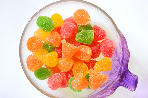 Photograph of colorful sugar coated gumdrops, jellybeans, jujuba or jujubes in a glass bowl isolated against plain, white background shot from top. A hot favorite with kids and some grownups too.