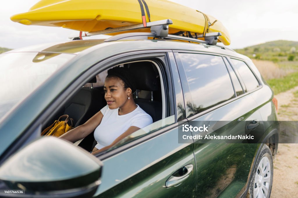 On the way to the lake Photo of a young woman in a car on the way to the lake. The kayak is on the roof of the car. Road Trip Stock Photo