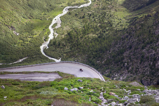 Mountain road, view on serpentine road on mountain pass and beautiful alps landscape. Motorcycle driver on a bend from above with green summer valley of the river. Furka Pass route in swiss alps.