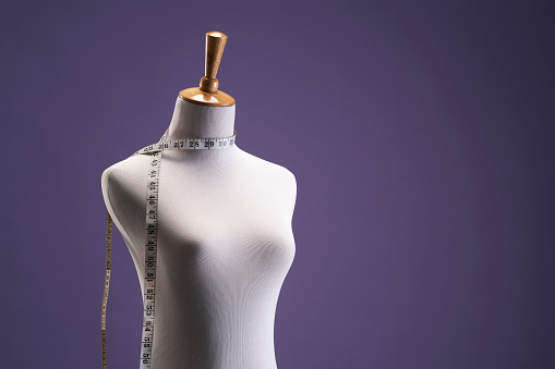 deskmaker's mannequin with tape measure against purple background