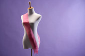 dressmaker's mannaquin with ribbon sash against purple background