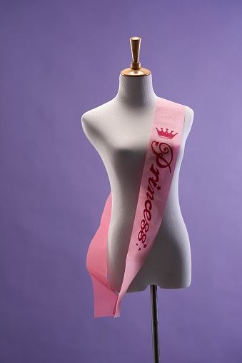 dressmaker's mannaquin with ribbon sash against purple background