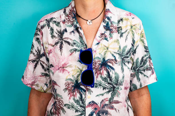 primo piano di occhiali da sole blu appesi alla camicia hawaiana di un uomo che indossa una collana. - camicia hawaiana foto e immagini stock