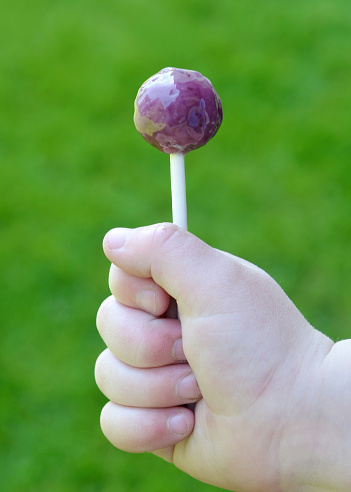 Closeup of a 3 year old boy holding his lollipop in the sunshine.
