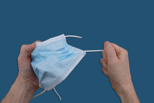 istock Man's hands stretching a used hygienic mask on a blue background. 1401772175