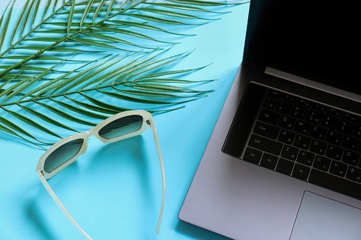 Working on the beach while on vacation concept photo. Online job, education image. Open laptop, sunglasses and palm leaves top view