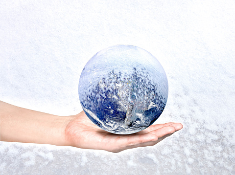 Extremely weather swing of climate change concept, hand holds cold earth on white snow background, selective focus. A dramatic frozen planet on human's palm, global warming issue for future people.