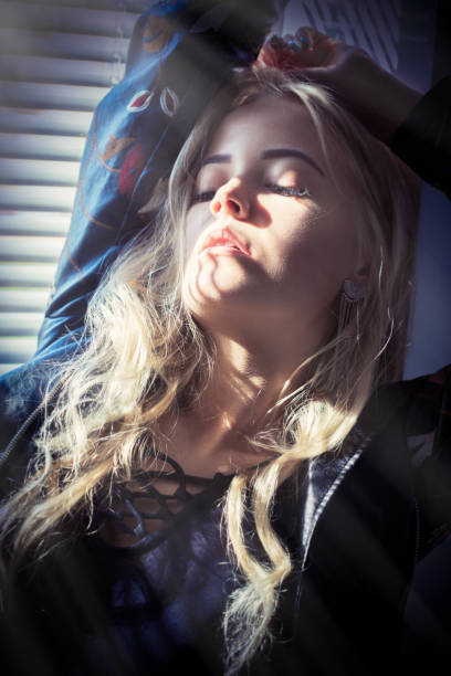 sensual girl with closed eyes sitting on window in sunlight with blinds