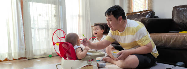 Single father feeding his son at home Asian father feeding his baby boy son with a spoon in the living room at home, they enjoy togetherness emotional series stock pictures, royalty-free photos & images