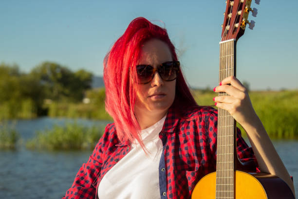 Blonde woman  playing guitar besides a lake