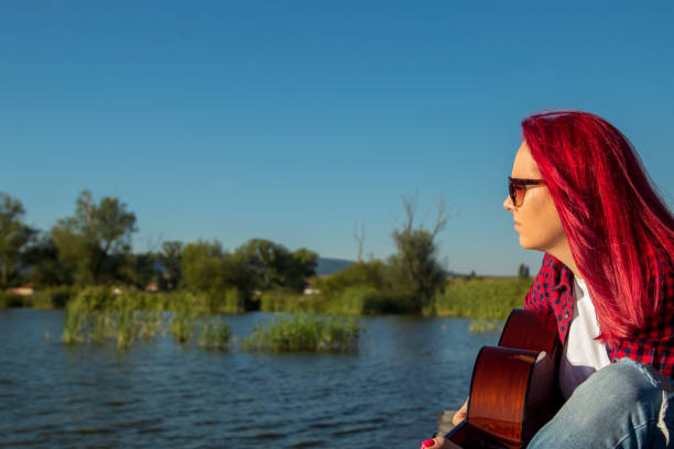Blonde woman  playing guitar besides a lake