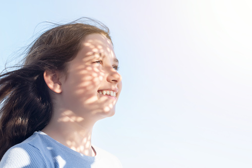 Young blue-eyed Caucasian girl smiling and looking at the horizon with shadows on her face. Gesture of happiness and well-being