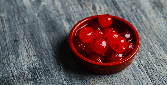a brown earthenware bowl with some maraschino cherries, on a gray rustic wooden table, in a panoramic format to use as web banner or header