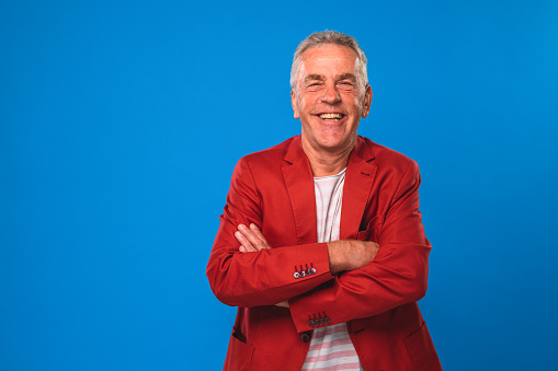 Studio portrait of Caucasian man with grey hair. Front view of smiling senior man wearing red blazer and crossing arms.